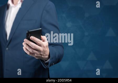 Online business. businessman holding mobile cellphone man using smart phone on dark blue background. man in a suit is holding a phone. cellular techno Stock Photo