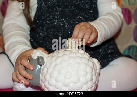 Little girl throwing money to her piggy bank Stock Photo