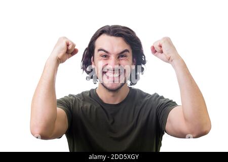 Pleased young man, long curly hair style, celebrates success hysterical and passionate. Guy keeps fists tight, raise hands up clenching teeth, isolate Stock Photo