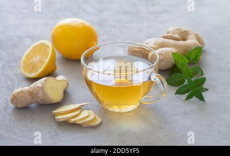 Transparent cup of healthy hot ginger tea with mint and lemon on stone table Stock Photo