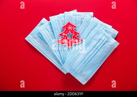 Medical protective mask with a toy of shape christmas tree on a red background. Christmas and Happy New Year concept, medical concept. Stock Photo