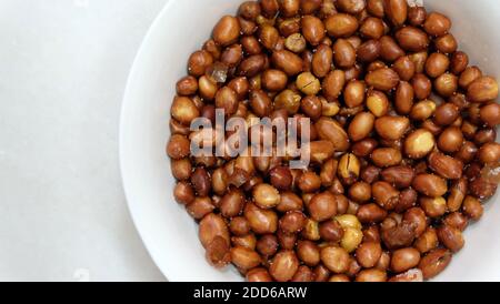 A bowl of fried peanuts with skin, lightly salted, in a white bowl. Top view. Stock Photo