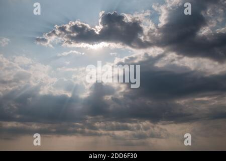 Sun rays on dramatic sky. Storm clouds and sun behind on sky background. Gray clouds of rain and storm with sunbeams. Stock Photo