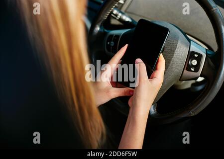 Over the shoulder close up view of young woman texting on mobile phone whilst driving and not concentrating on the road Stock Photo