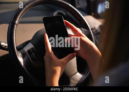 Over the shoulder close up view of young woman texting on mobile phone whilst driving and not concentrating on the road Stock Photo