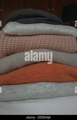 Stack of sweaters on the bed one on top of the other. Different colors and textures to keep warm on cold days this Christmas 2020. Stock Photo