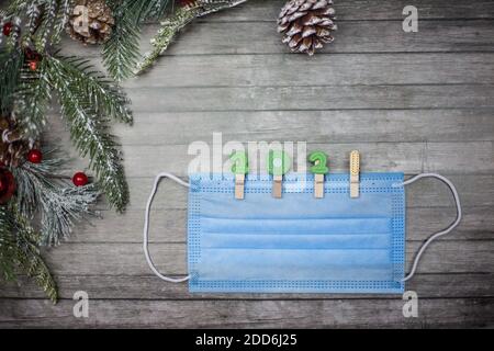 Medical mask with clothespins in the form of the numbers 2021 on a wooden background and New Year's branches. Copy space for text Stock Photo