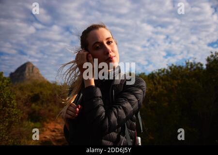 Portrait of young woman on vacation wearing backpack walking along path through countryside on blue sky day Stock Photo