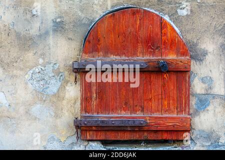 Arched window on an old stone wall, closed by wooden shutters with large iron hinges and a lock. From the window of the world series. Stock Photo