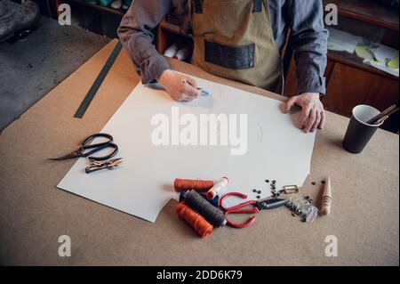 In a family shoe shop a young apprentice works with paper to create a pattern for shoes. Stock Photo