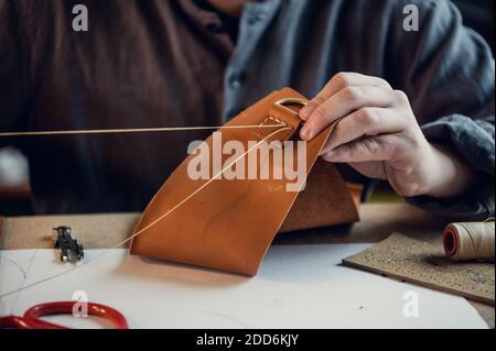 Close-up photo the hands of a skilled shoemaker make a bag from a piece of genuine leather. Stock Photo