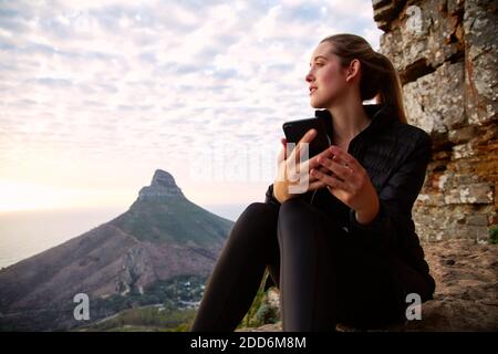 Young woman on vacation walking along coastal path at sunset or sunrise checking messages on social media with mobile phone Stock Photo