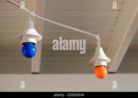 Two led lamps hanging at a white ceiling. Decorative blue and red light bulbs are connected with a white cable. Stock Photo