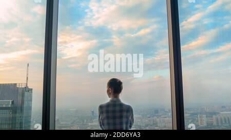 Pensive woman looking at cityscape through window of skyscraper - back view Stock Photo