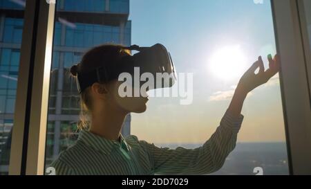 VR concept - young woman using virtual reality headset against skyscraper window Stock Photo
