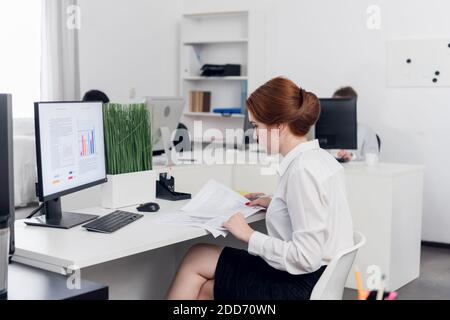Girl Manager in a white blouse at the computer calculates the profit and loss of the company, builds charts Stock Photo