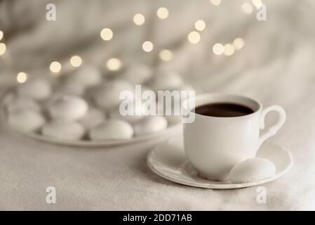 White cup of coffee with meringues on soft blanket. Bokeh lights on the background. Cozy winter still life. Stock Photo