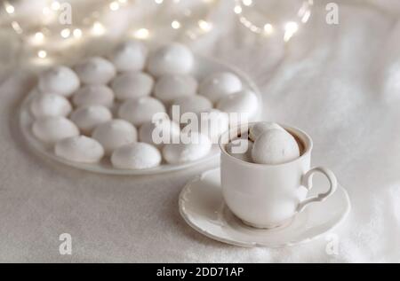 White cup of coffee with meringues on soft blanket. Bokeh lights on the background. Cozy winter still life. Stock Photo