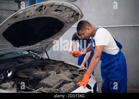 Two male mechanics in uniform inspect a car engine Stock Photo