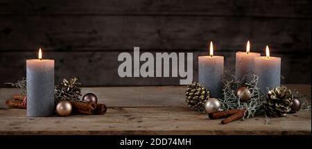 Burning candles and Christmas decoration like cones, baubles and cinnamon sticks on a rustic wooden table against a dark background, panoramic format, Stock Photo