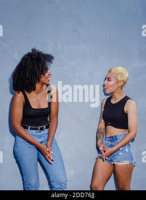 two laughing young women in identical clothes stand laughing together Stock Photo