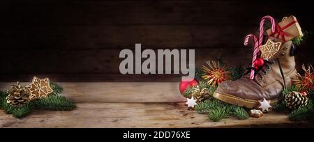 Old hiking boot filled with sweets, gifts and Christmas decoration, German tradition on Nicholas or Nikolaus day at 6th December, dark rustic wooden b Stock Photo