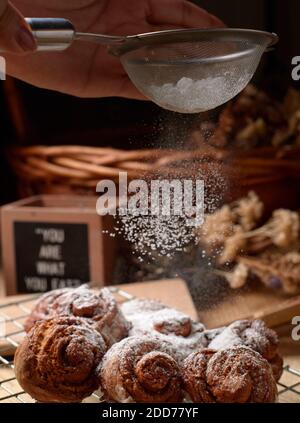 Close Up view chef sprinkle icing sugar over the cinnamon rolls Stock Photo