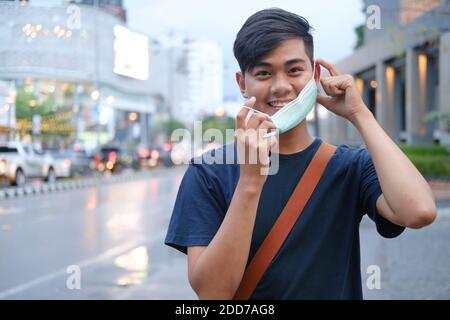 Young man during pandemic isolation at city. Removing mask from face. Coronavirus and New normal concept. Stock Photo