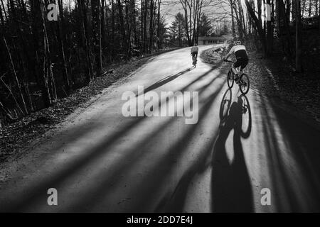 Bicyclists cast long shadows on a late fall (November) day, East Montpelier, VT, New England, USA. Stock Photo