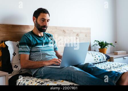 Millennial man working on the laptop at home on bed Stock Photo