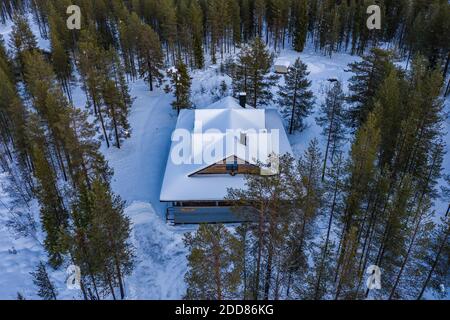 Aerial of wooden cabin in the remote forest, with snow covered woods and trees landscape in Lapland, Finland, Europe Stock Photo