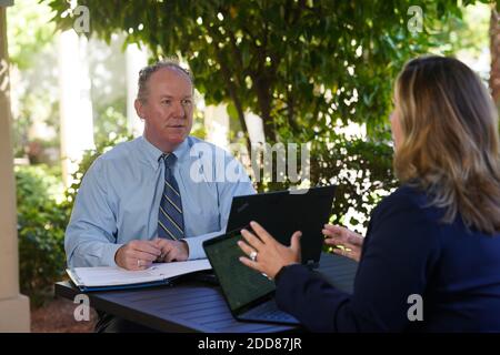 A businessman conducts a meeting with a woman outside in a casual setting. Stock Photo