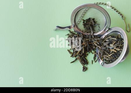close up view of light green table surface with an open tea filter and dry leaves of green tea on the top Stock Photo