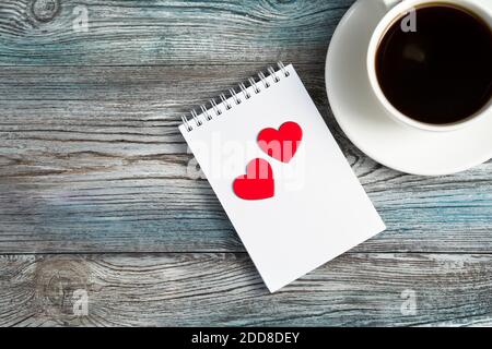Ceramic white coffee mug and two red hearts on a Notepad. Stock Photo