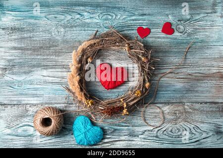 Red and blue hearts and a wreath of natural branches and dry grass on a gray-blue wooden background. Stock Photo