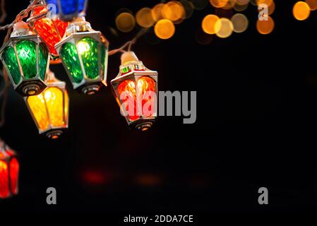 Glowing Xmas lights in black night. colorful Ffairy christmas lights with vintage lantern shaped lamps . Stock Photo