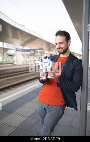 Smiling businessman looking at robot while standing on railroad platform Stock Photo