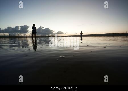 Silhouette tourists at beach with reflection in water against sky during sunset Stock Photo