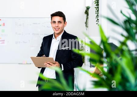 Smiling male professional writing on clipboard while standing by cabinet at office Stock Photo