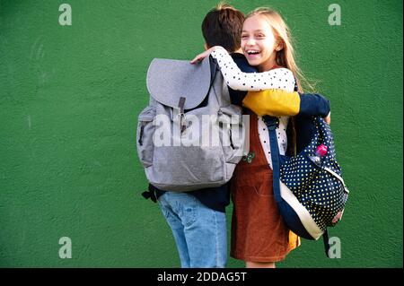 Brother and sister embracing each other while standing against green wall on sunny day Stock Photo