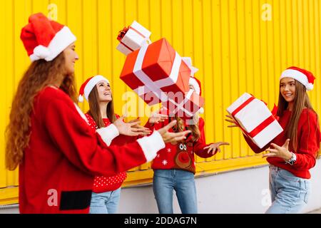 Excited, rejoicing group of friends wearing santa claus hats having fun and tossing christmas presents on yellow wall Stock Photo