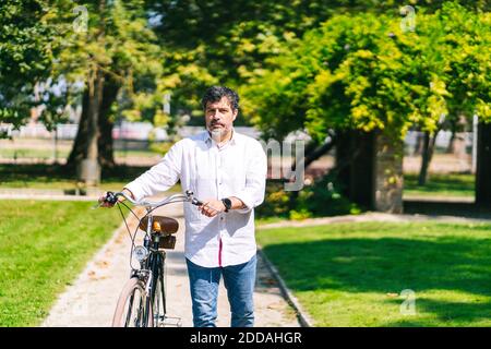 Mature man with bicycle walking on walkway in park on sunny day Stock Photo