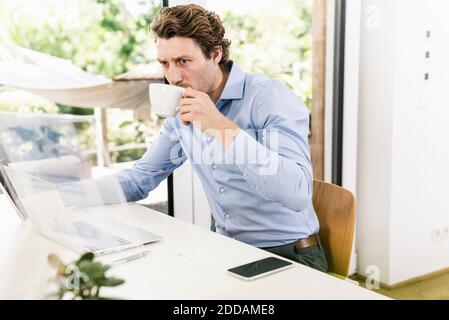 Man working on laptop while drinking coffee sitting in office Stock Photo