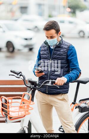 Young man with bicycle using smart phone while standing on street Stock Photo