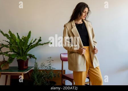 Beautiful female model wearing jacket looking down while standing at home Stock Photo