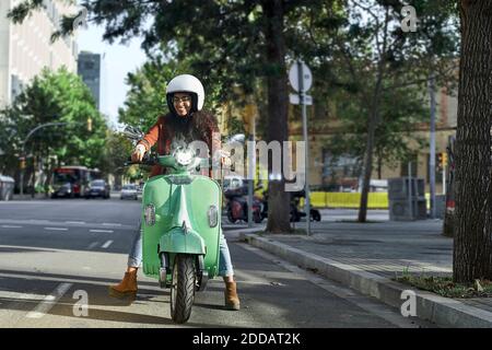 Smiling young woman riding motor scooter on street in city Stock Photo