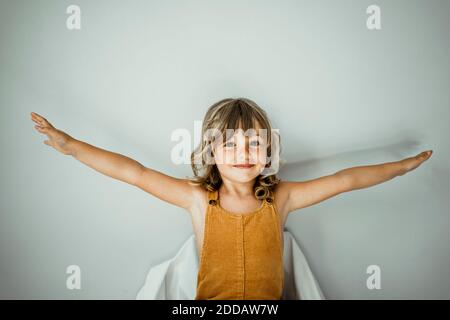 Little girl with arms outstretched standing against wall at home Stock Photo