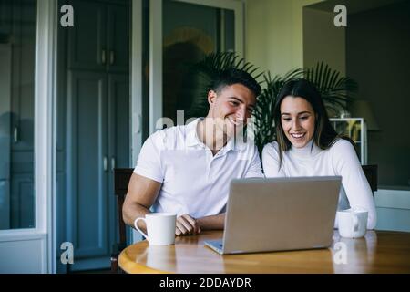 Boyfriend and girlfriend having coffee while using laptop sitting at home Stock Photo