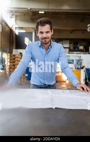 Smiling man leaning on table while working  at factory Stock Photo
