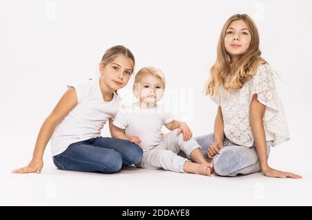 Blond sisters sitting against white background in studio Stock Photo
